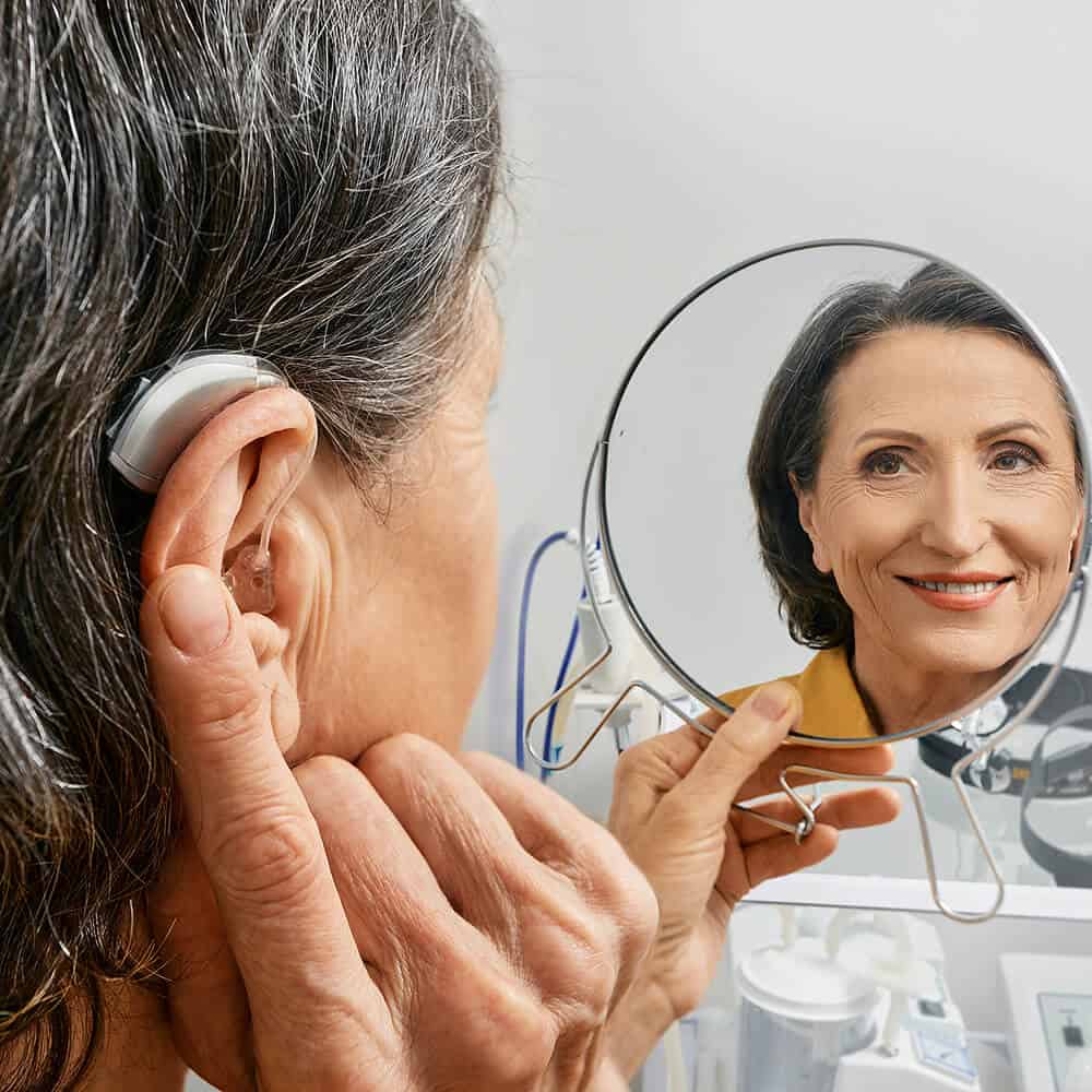 woman looking in mirror at self with hearing aid